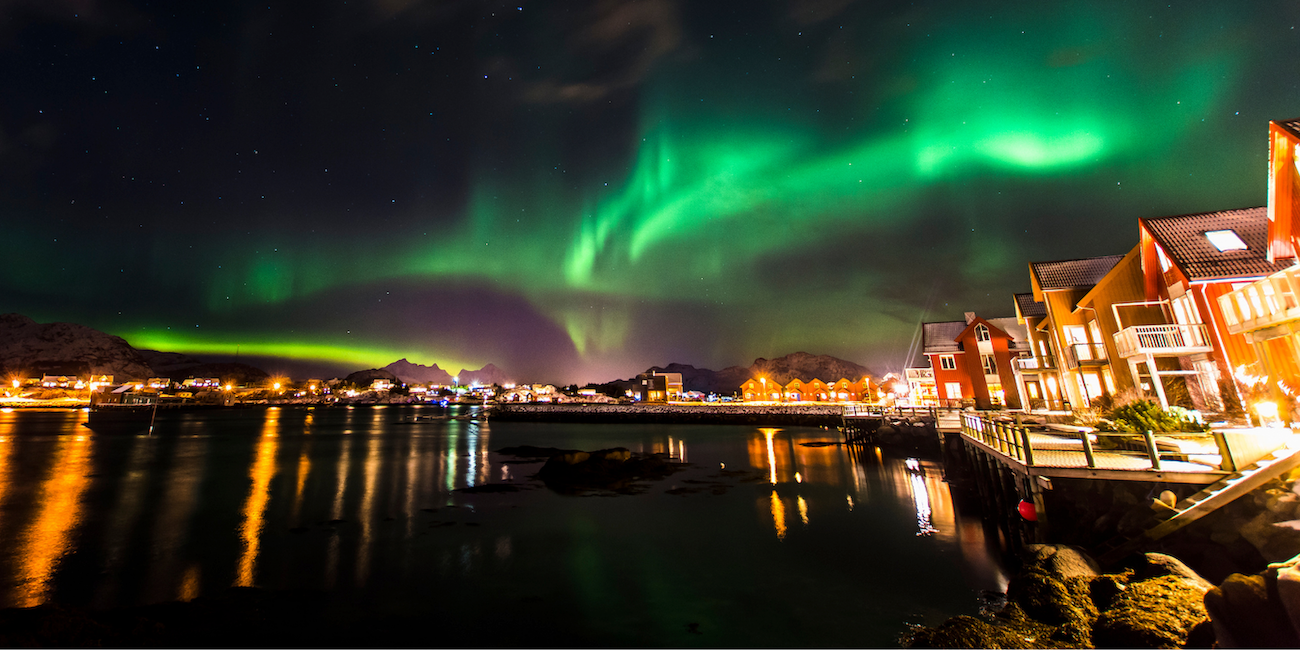 Northern Lights glowing above a cruise ship sailing through Arctic waters near snow-covered mountains during winter.